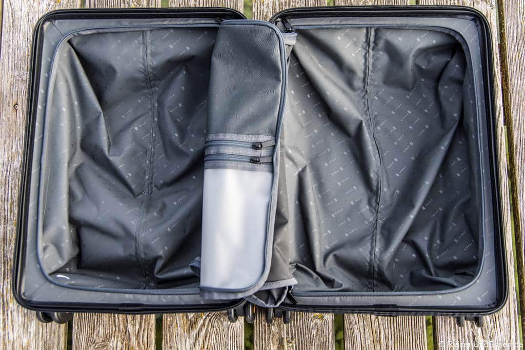 Ein offener, leerer schwarzer Handgepäck-Koffer für Kurzreisen mit einer grauen Trennwand mit Reißverschluss steht auf einer Holzfläche. Das Innere des Koffers weist ein dezentes Muster auf und ist in zwei Bereiche unterteilt, von denen einer teilweise durch die Trennwand mit Reißverschluss verdeckt ist.